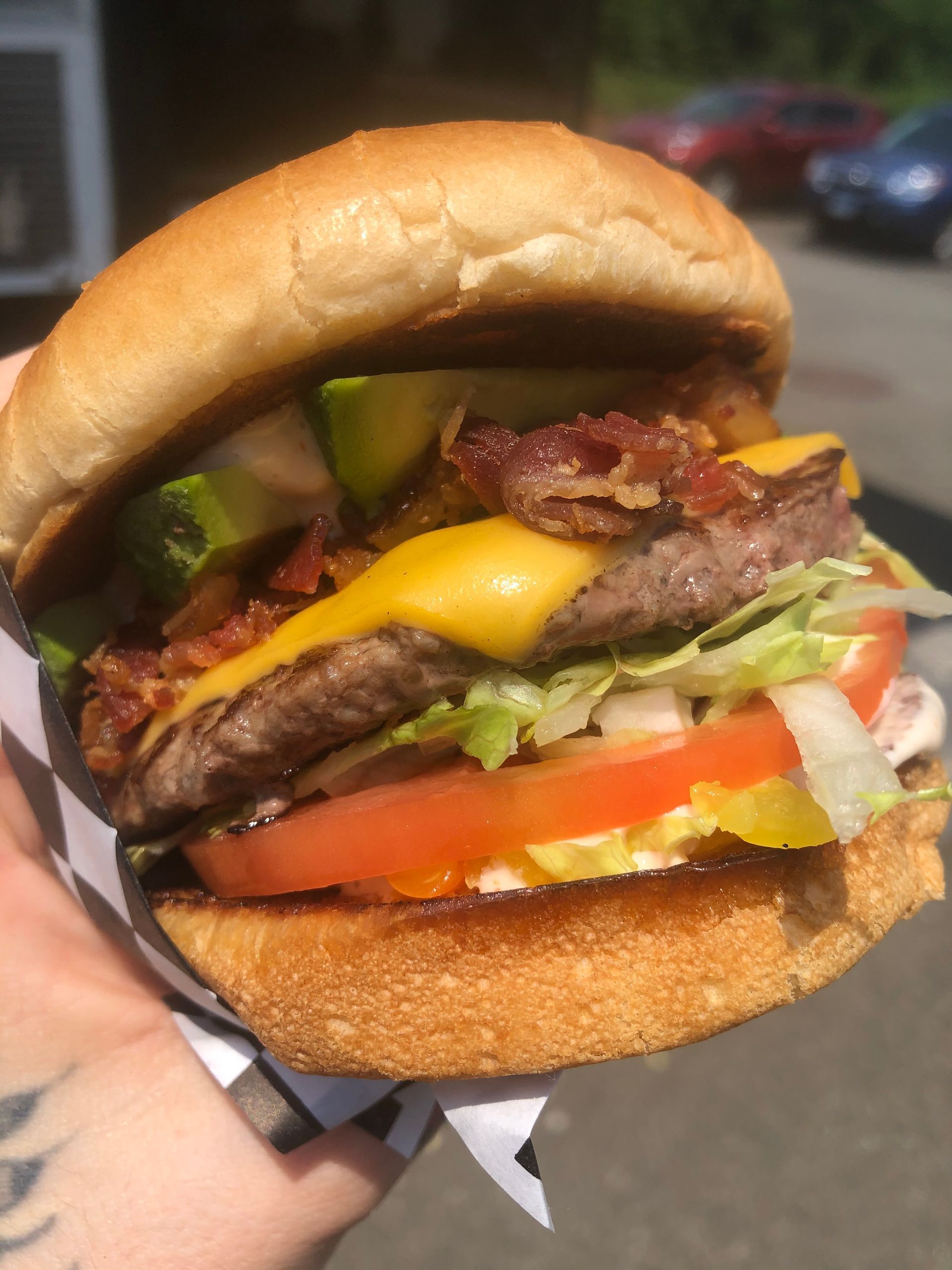 A person is holding a hamburger with cheese , lettuce , tomato and bacon.