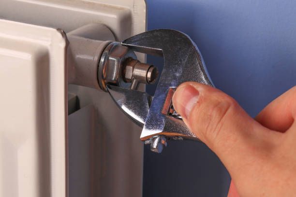 A person is fixing a radiator with a wrench.