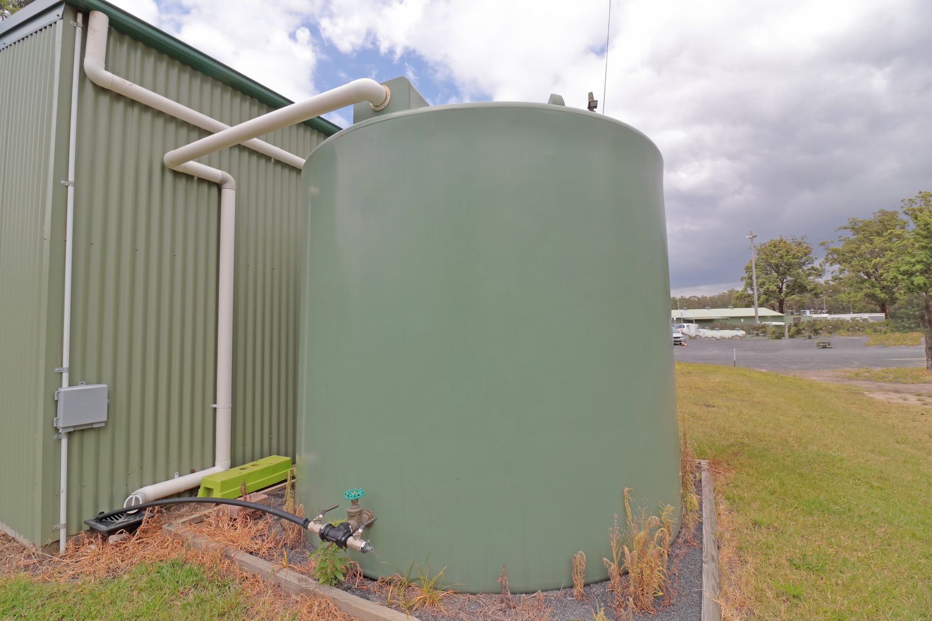 A green water tank is sitting next to a green building.