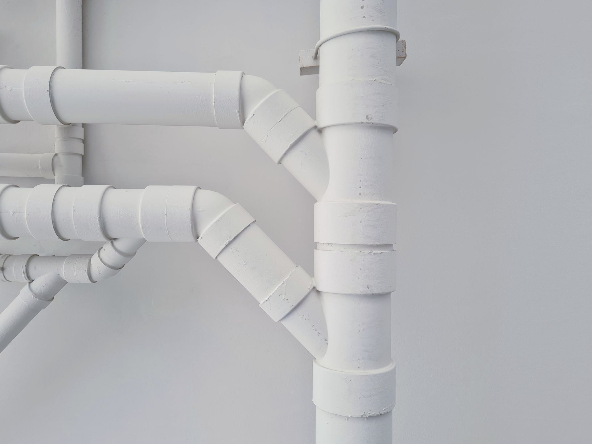 A bunch of white pipes are connected to each other on a white wall.