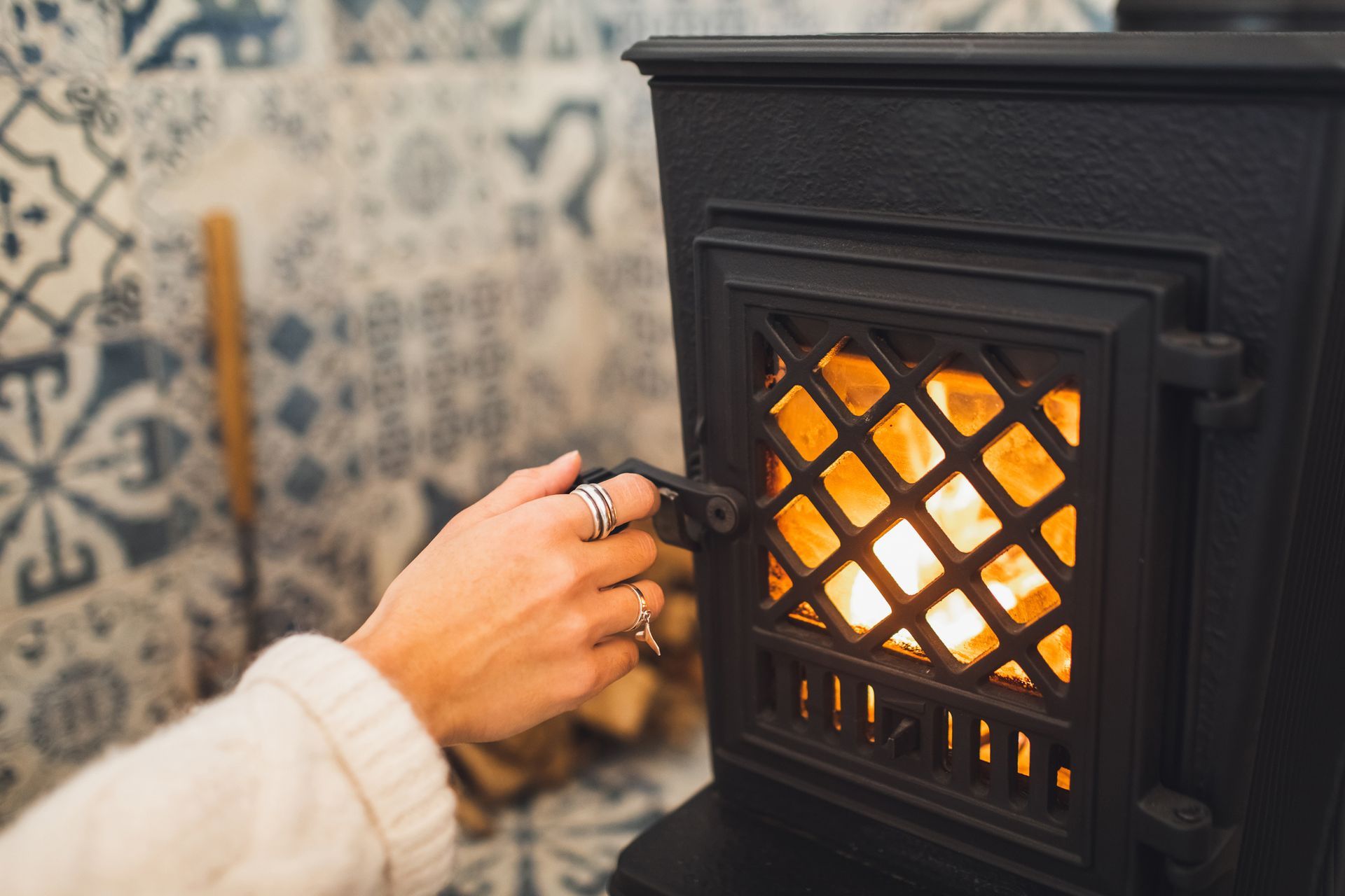 A person is lighting a wood stove with a ring on their finger.