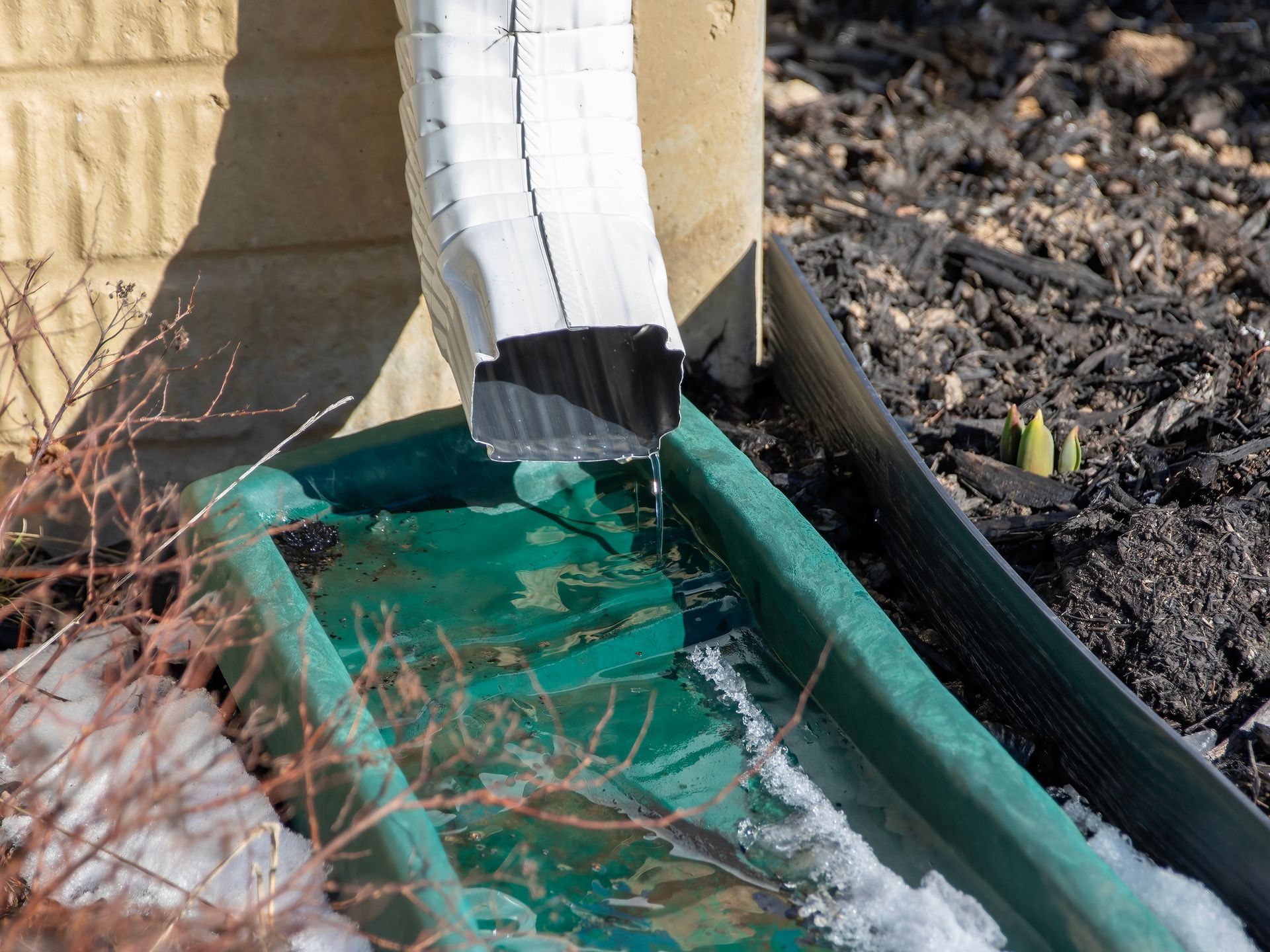 A gutter is draining water into a green container.