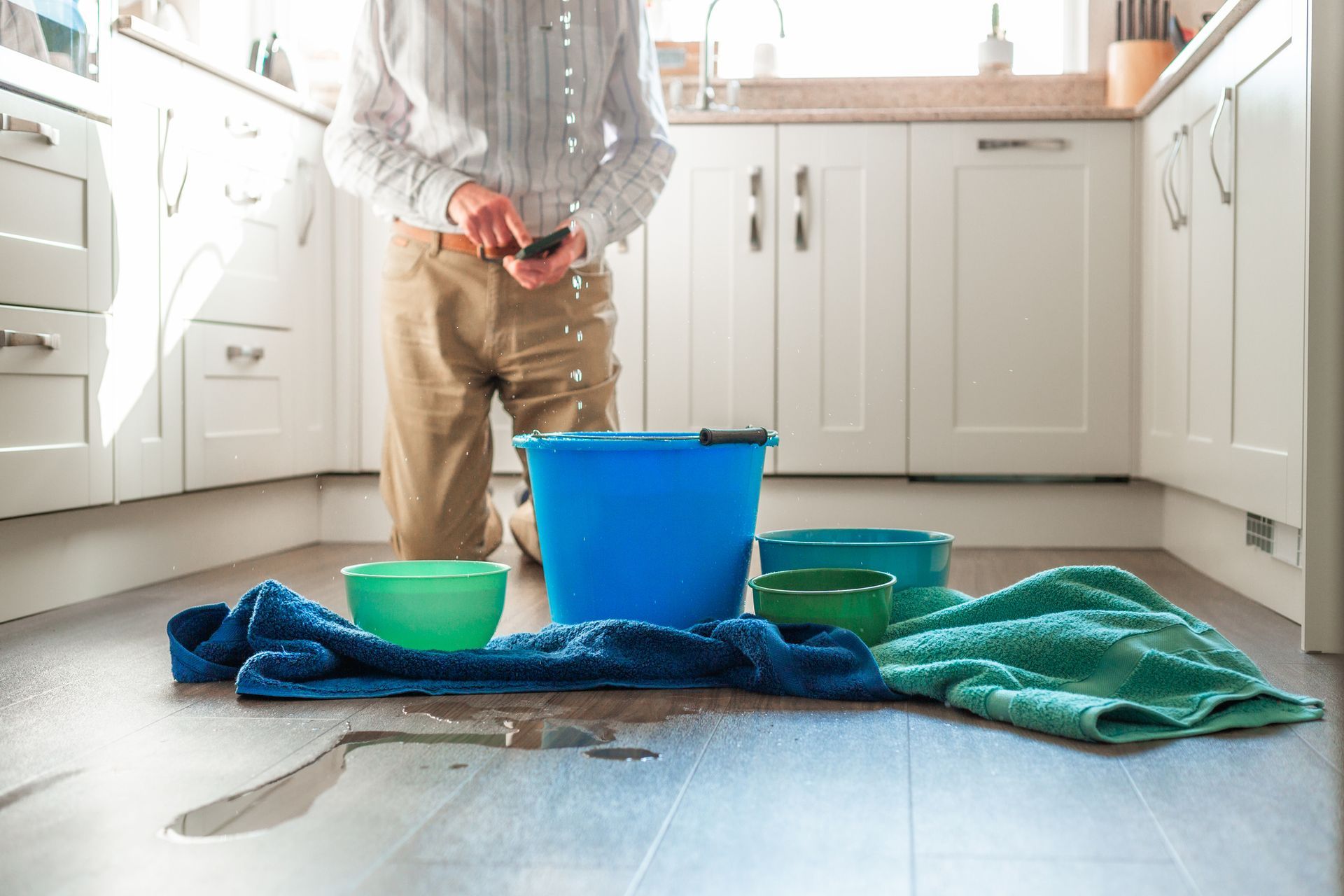 A man is kneeling in a kitchen next to a bucket of water.