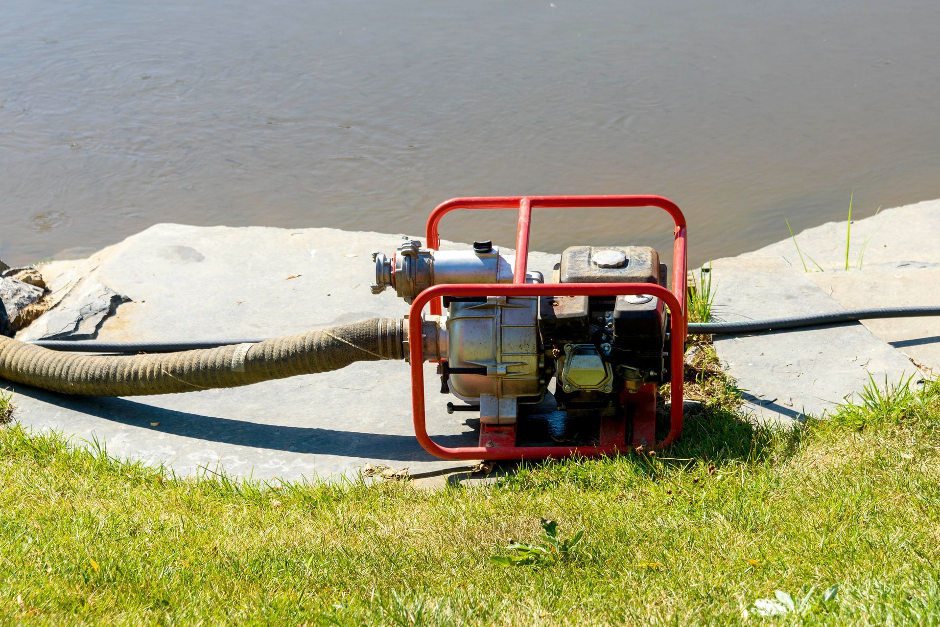 A water pump is sitting on the grass next to a body of water.