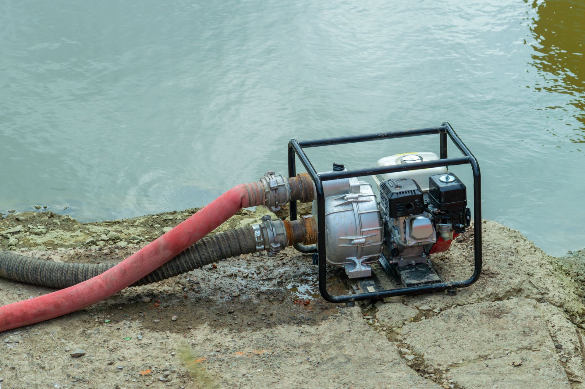 A water pump with a hose attached to it is sitting on a rock next to a body of water.