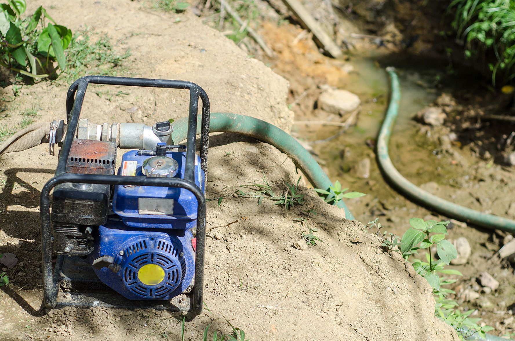 A blue water pump is sitting in the dirt next to a hose.