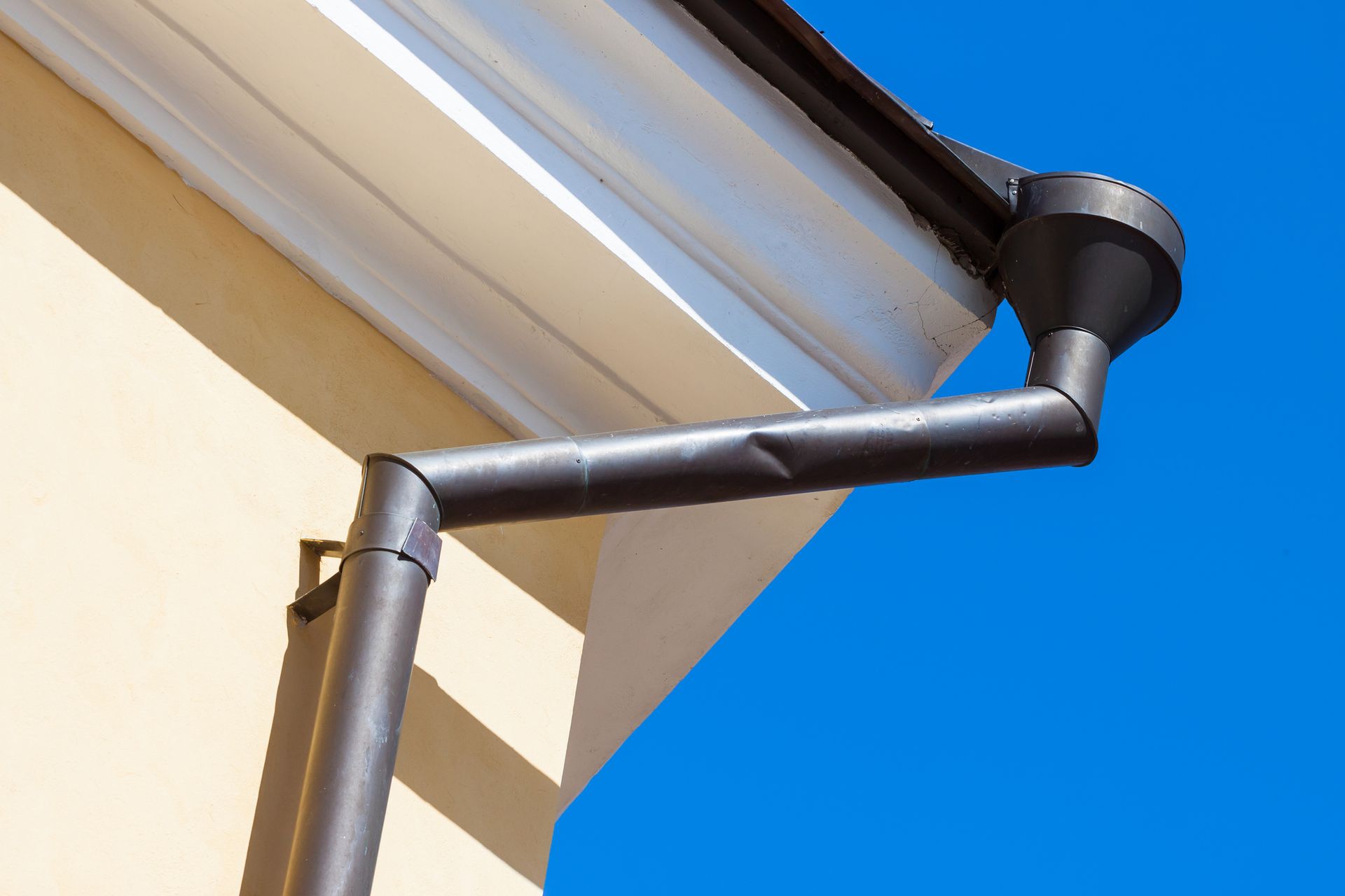 A gutter on the side of a building with a blue sky in the background.
