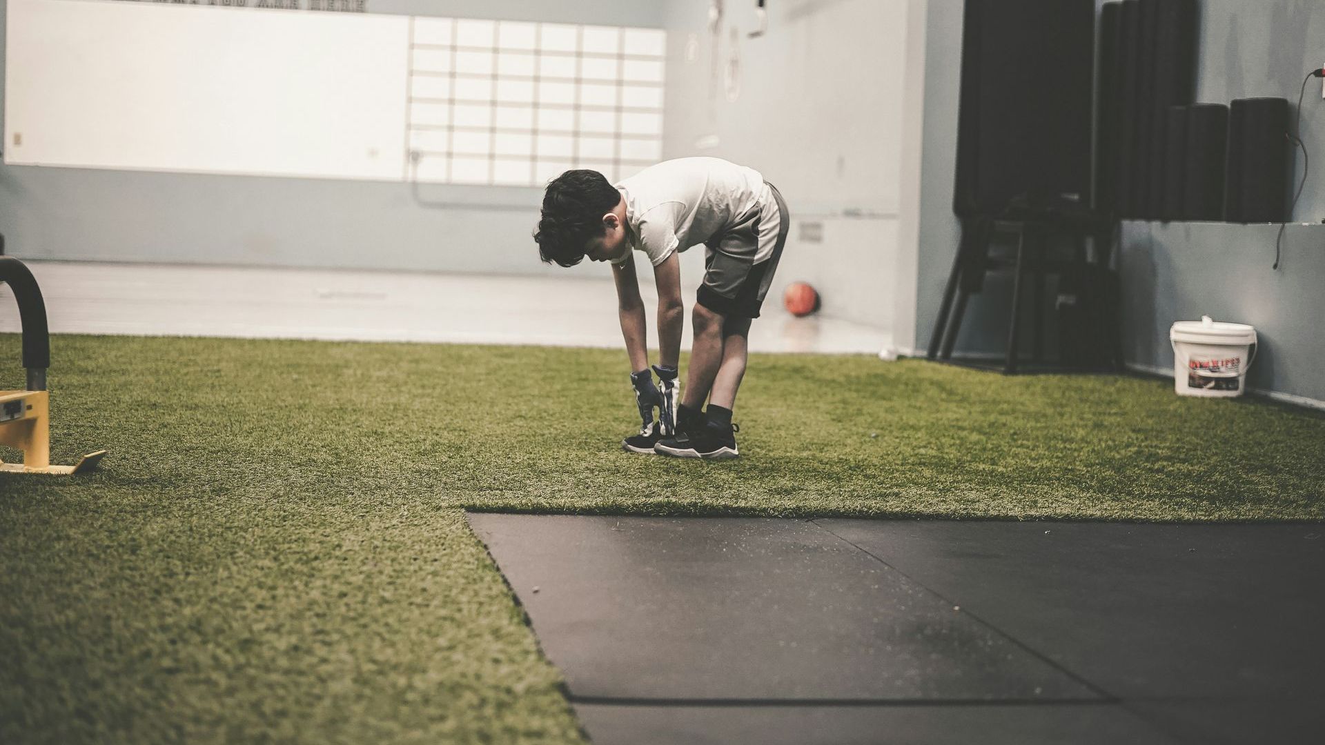 A young boy is bending over on the grass in a gym.