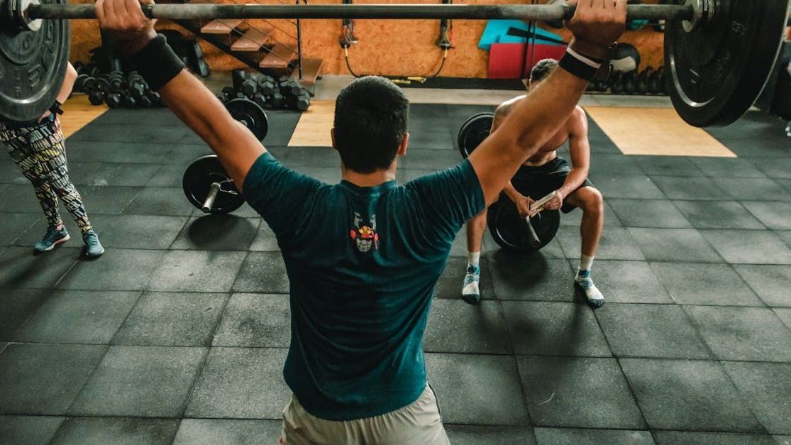 A man is lifting a barbell over his head in a gym.