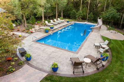 Blue pool with a slide surrounded by concrete and trees