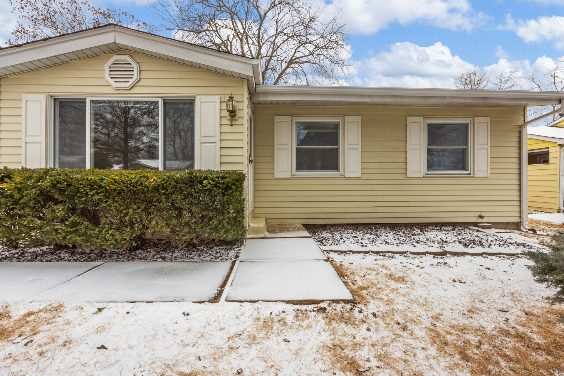 A yellow house with white shutters and a walkway in front of it