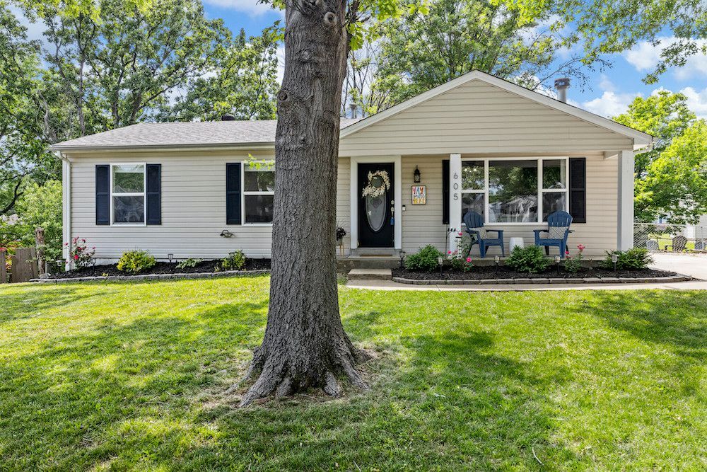 A white house with black shutters and a tree in front of it.
