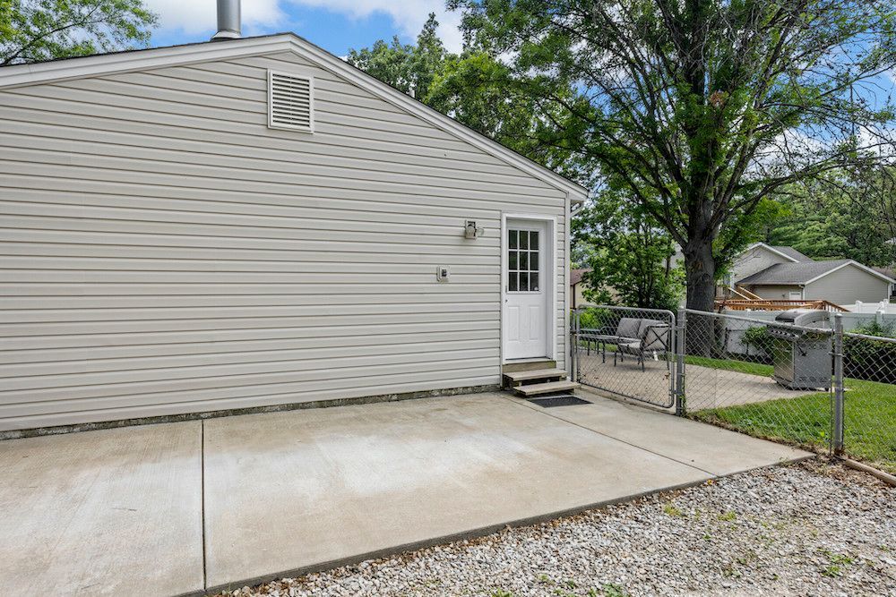 A white house with a concrete driveway and a fence in front of it.