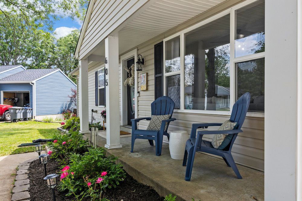 There are two chairs and a table on the porch of a house.