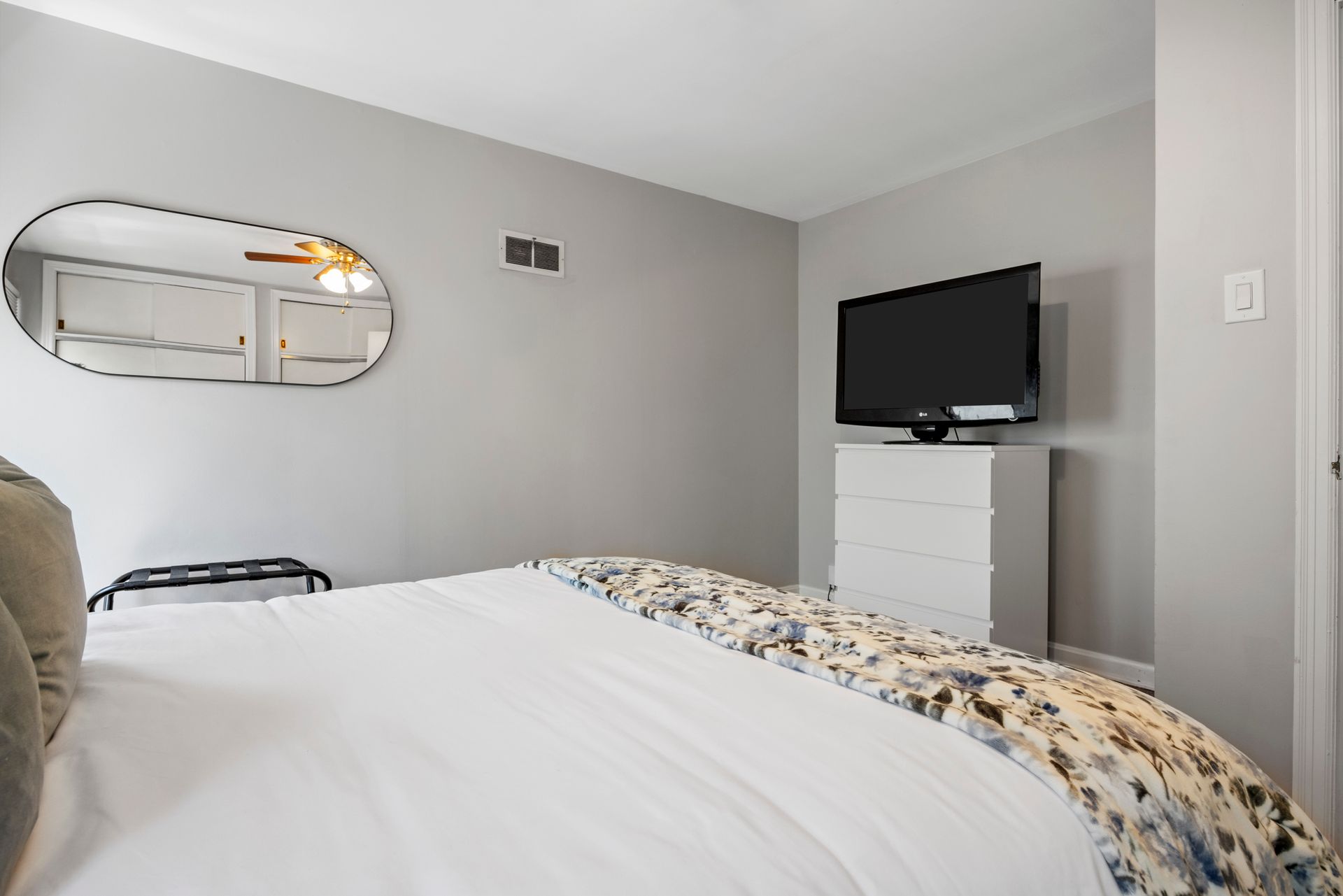 A bedroom with a bed , television , mirror and dresser.