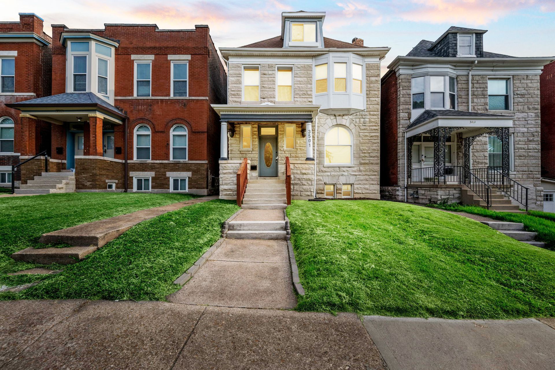 Row of historic brick and stone houses with green lawns and a cloudy sky.