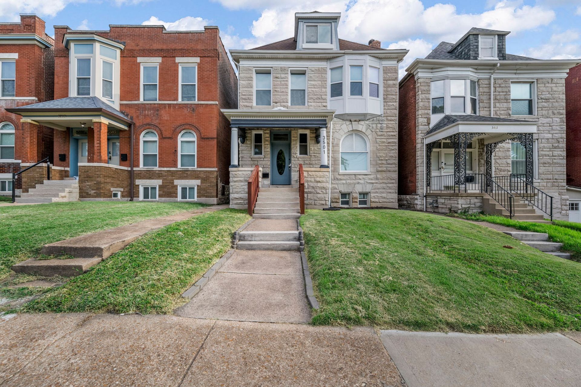 Row of multi-story brick and stone houses with front lawns and concrete walkways.