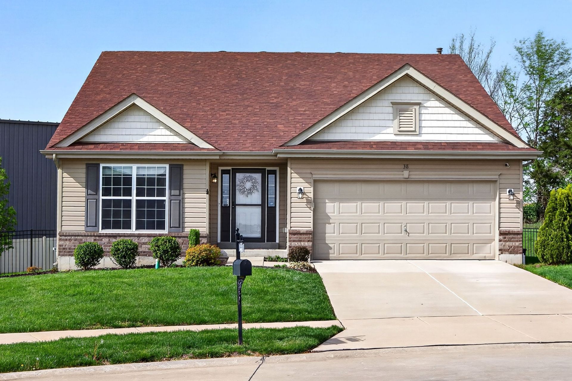 A single-story suburban house with beige siding, a reddish-brown roof, a double garage, and a green front lawn.