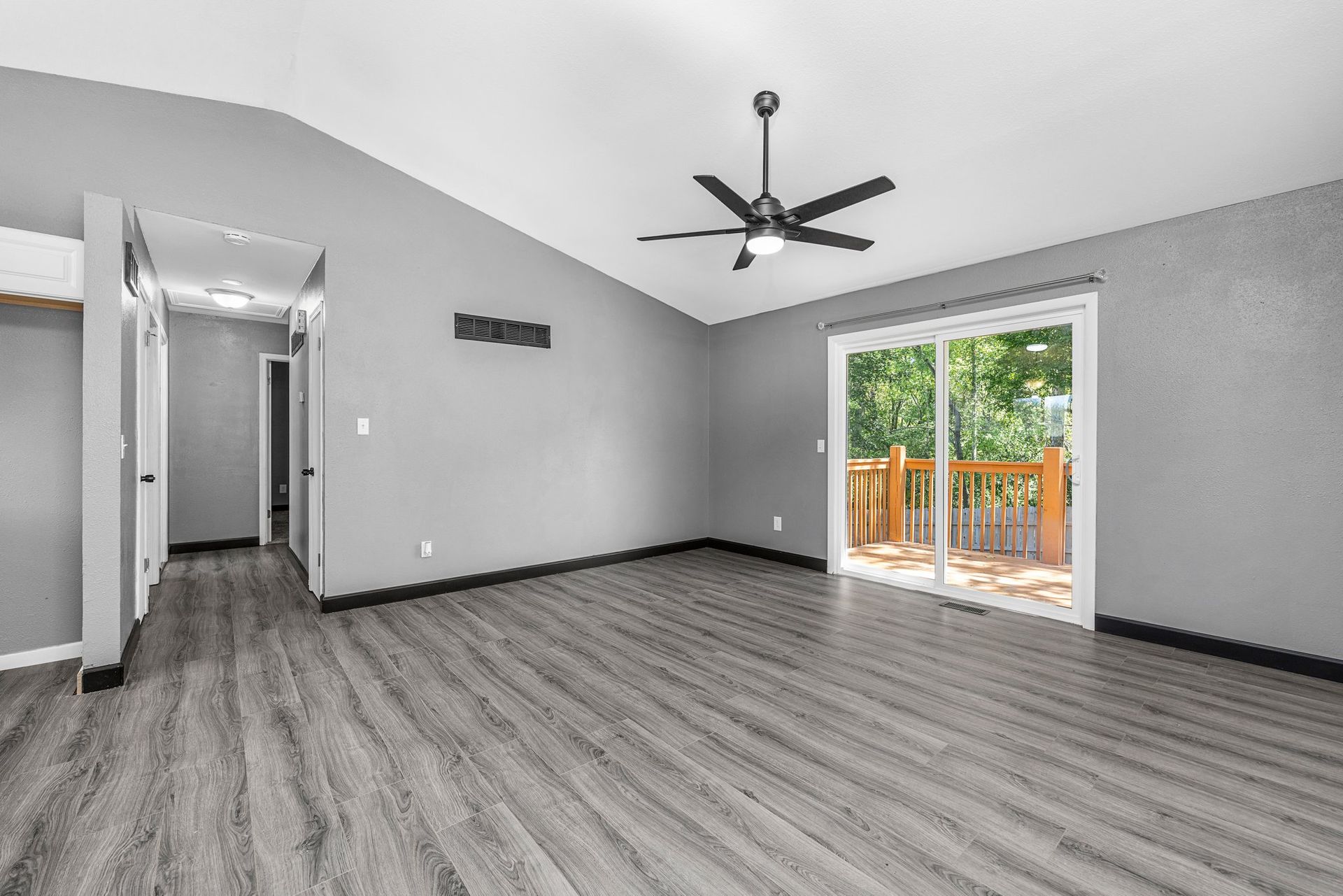 An empty living room with a ceiling fan and sliding glass doors.