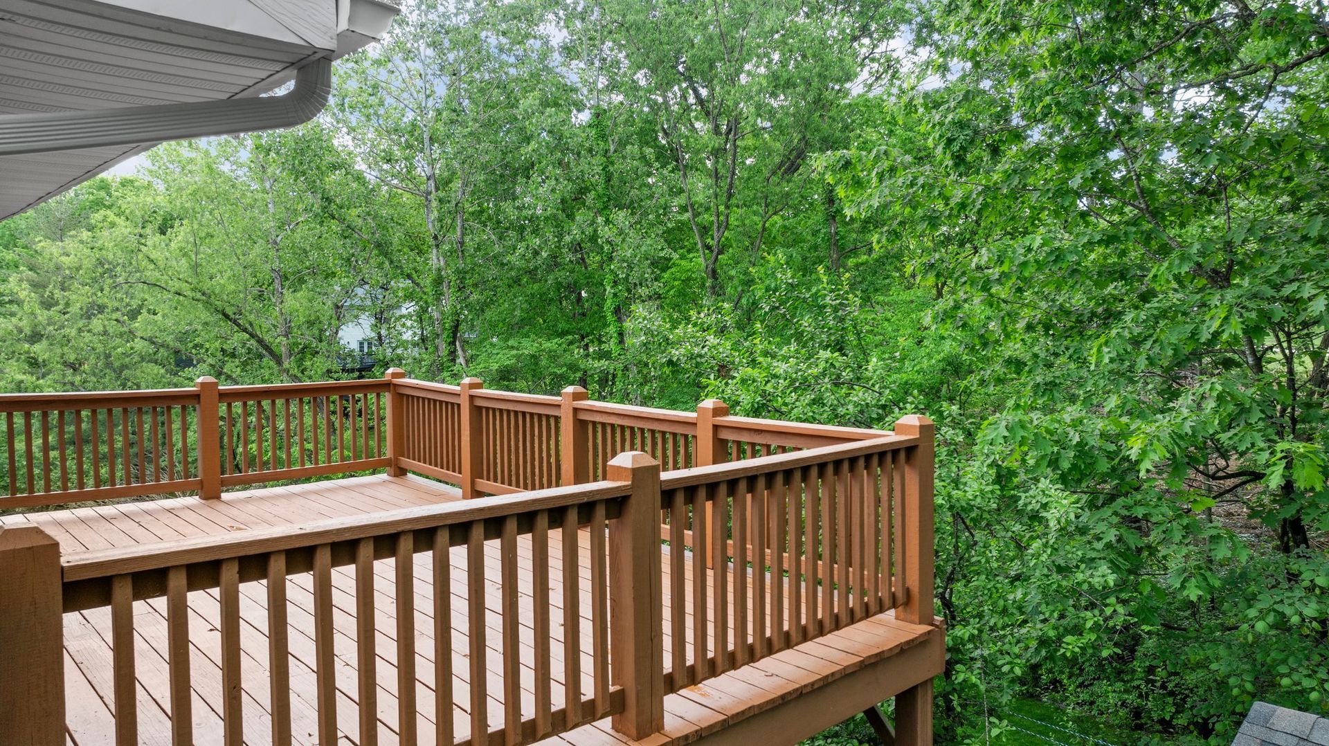 A wooden deck with a railing and trees in the background.
