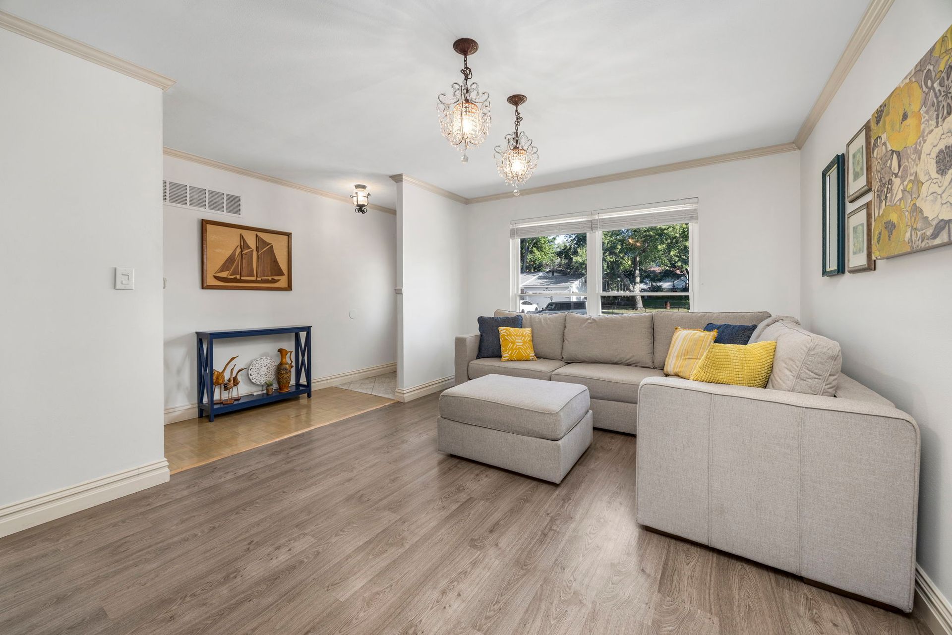 Living room with gray sectional, gray ottoman, and artwork. White walls and wood floors.