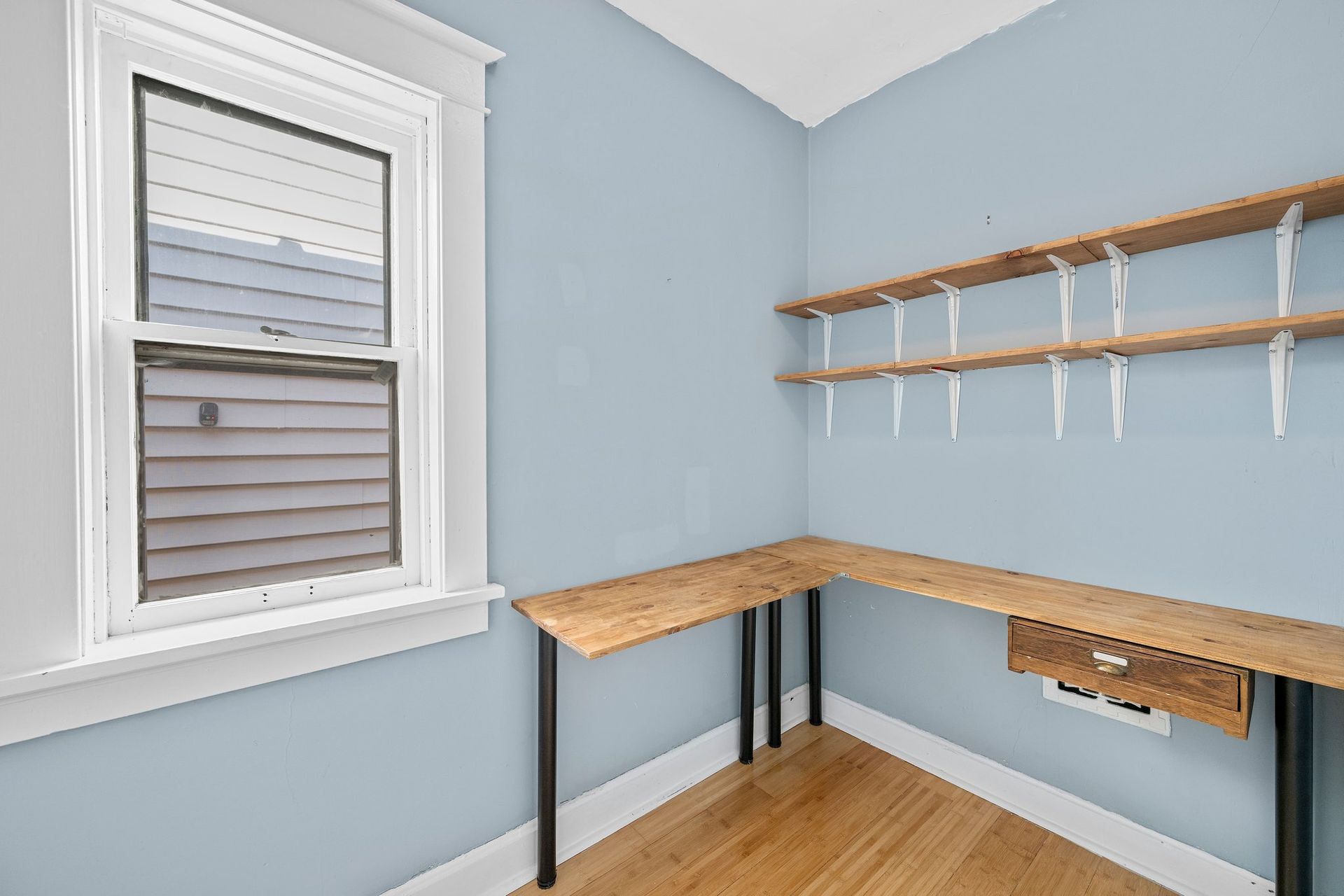 An empty room with a desk , shelves and a window.
