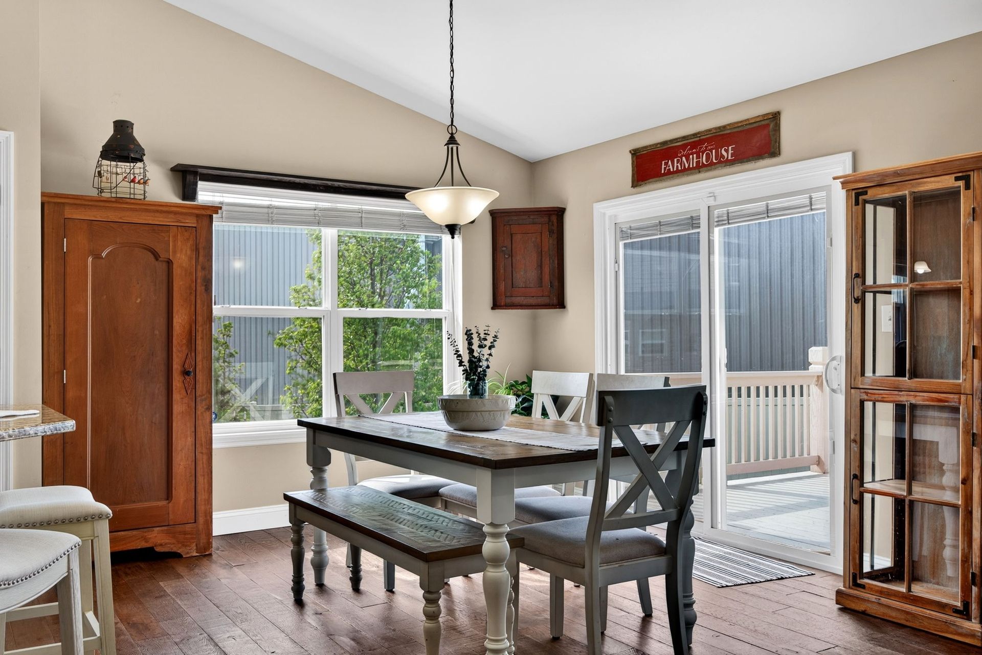 A dining area with a wooden table, bench, and chairs beneath a pendant light, flanked by two wooden cabinets.