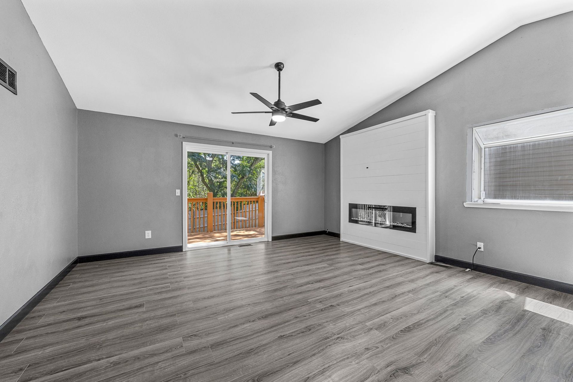 An empty living room with a ceiling fan and sliding glass doors.