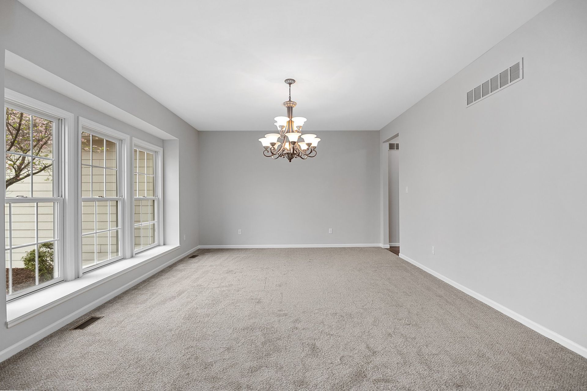 An empty living room with a chandelier and a lot of windows.