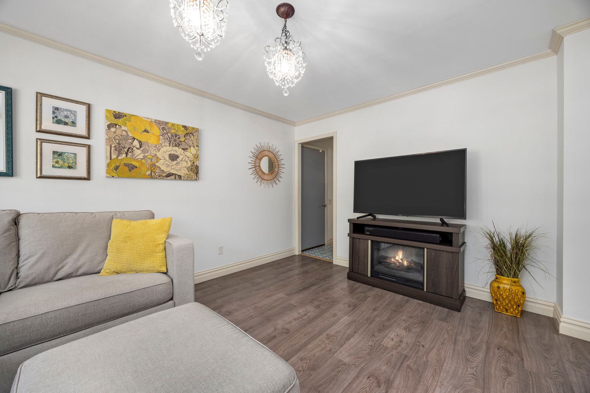 Living room with gray sofa, ottoman, TV, fireplace, art, and crystal chandeliers.