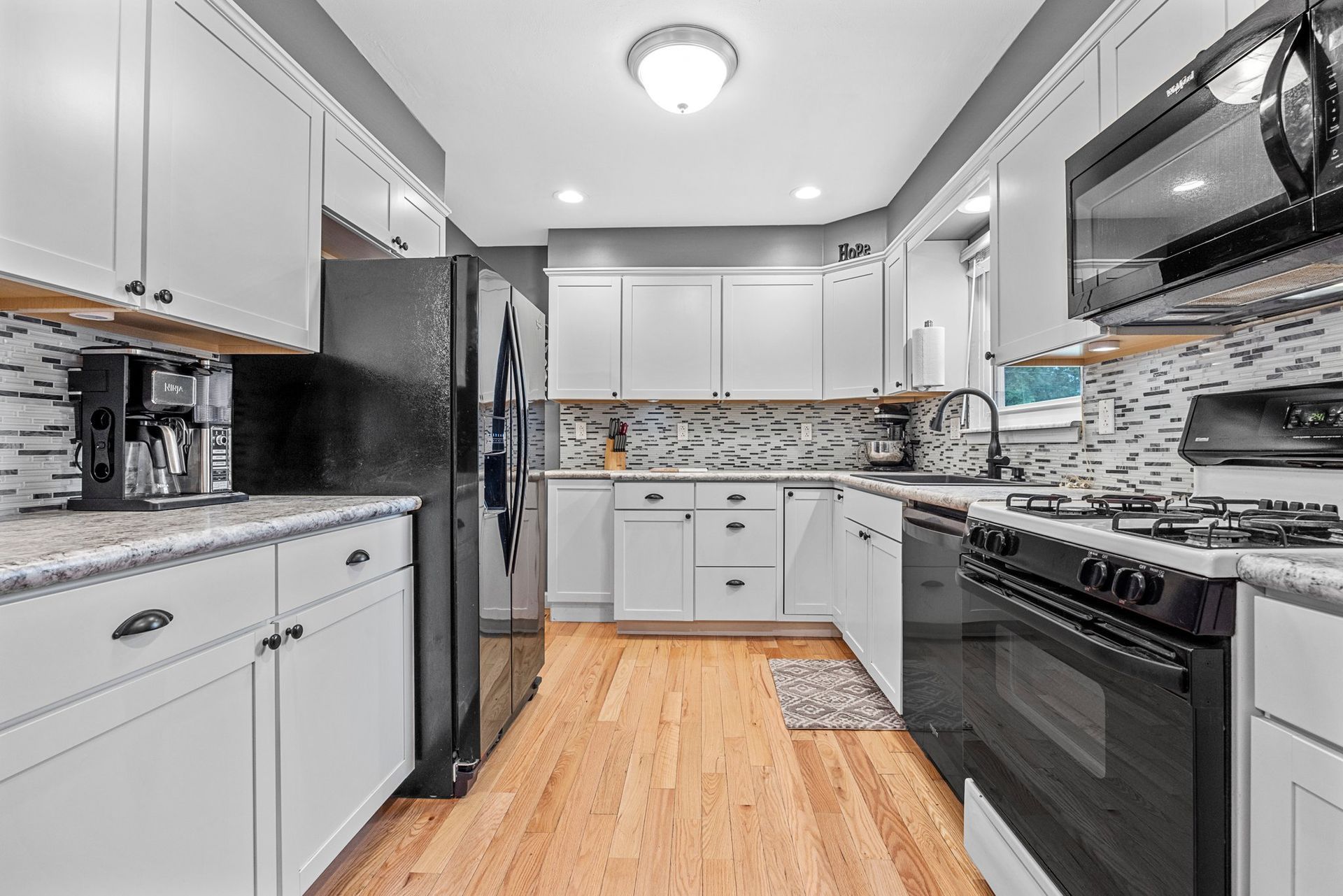 A kitchen with white cabinets , black appliances , and hardwood floors.