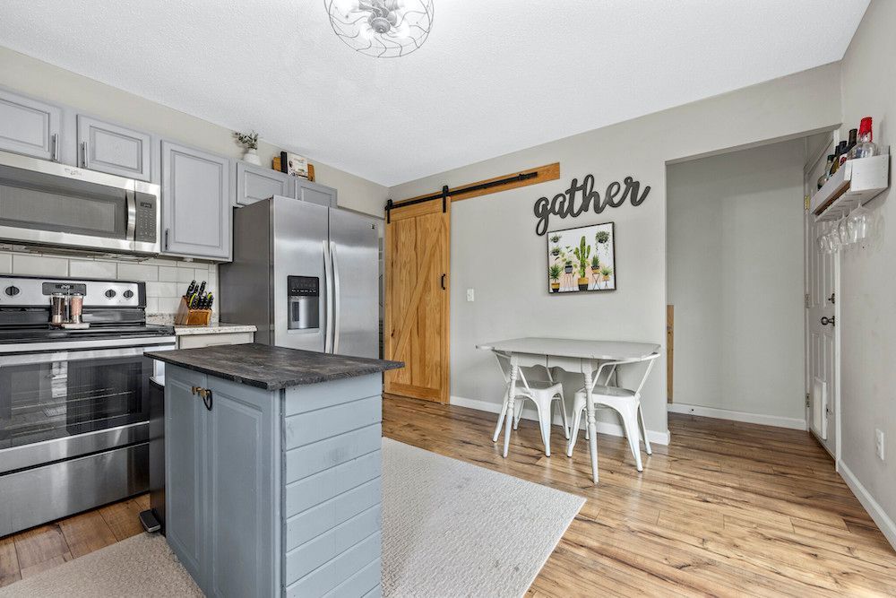 A kitchen with stainless steel appliances , a gray island , a table and chairs.