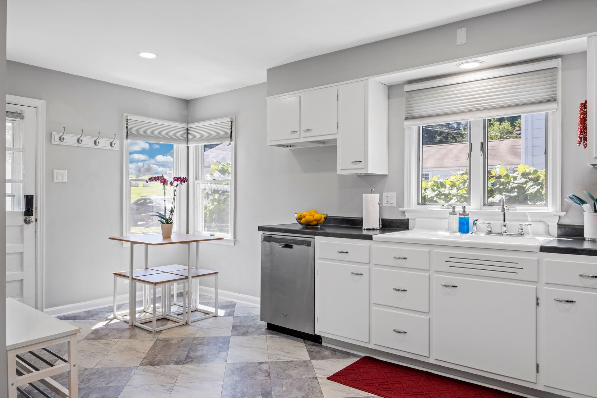 A kitchen with white cabinets , a stainless steel dishwasher , a table and chairs.