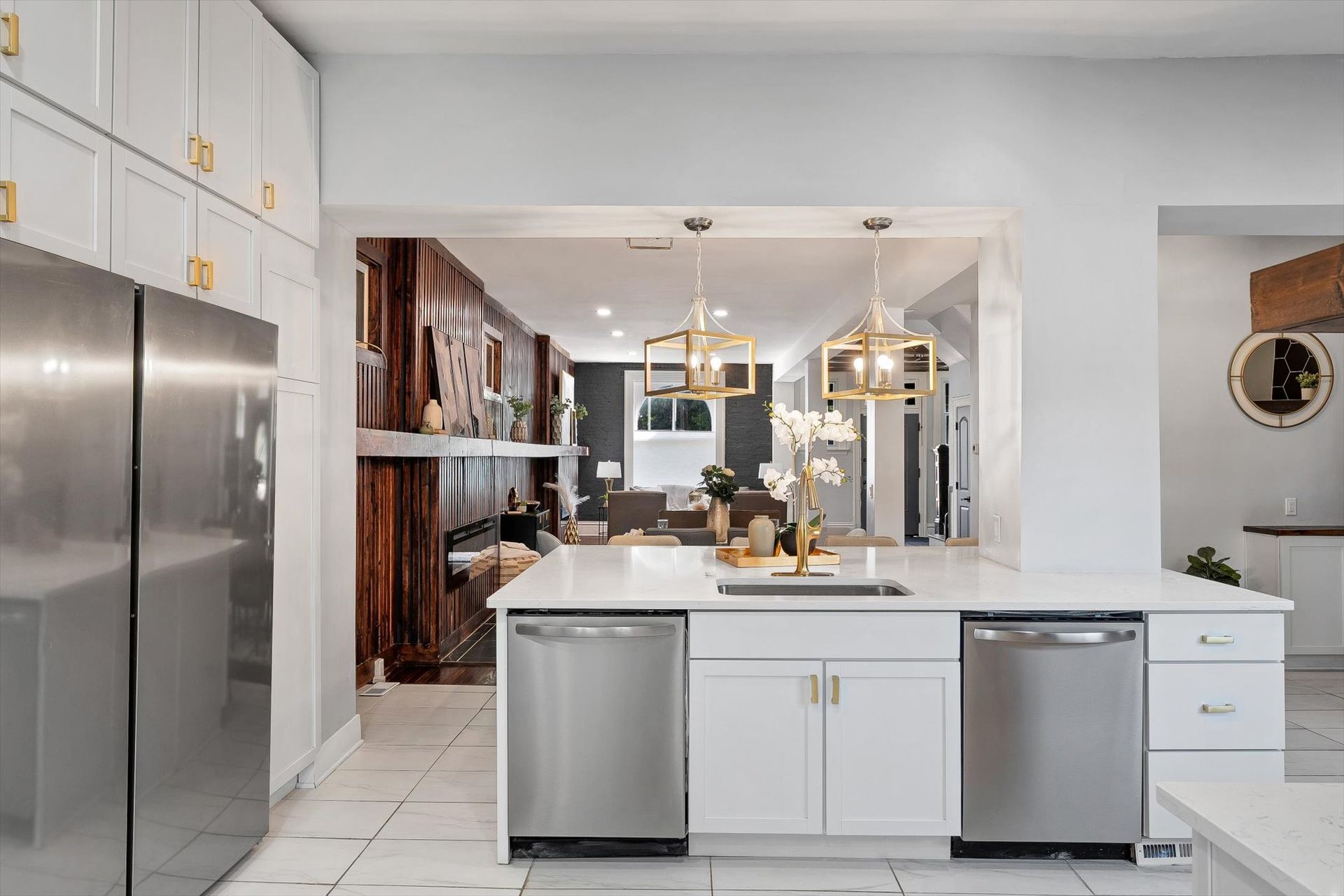 White kitchen with island, stainless steel appliances, and a view into a living area with warm-toned decor.