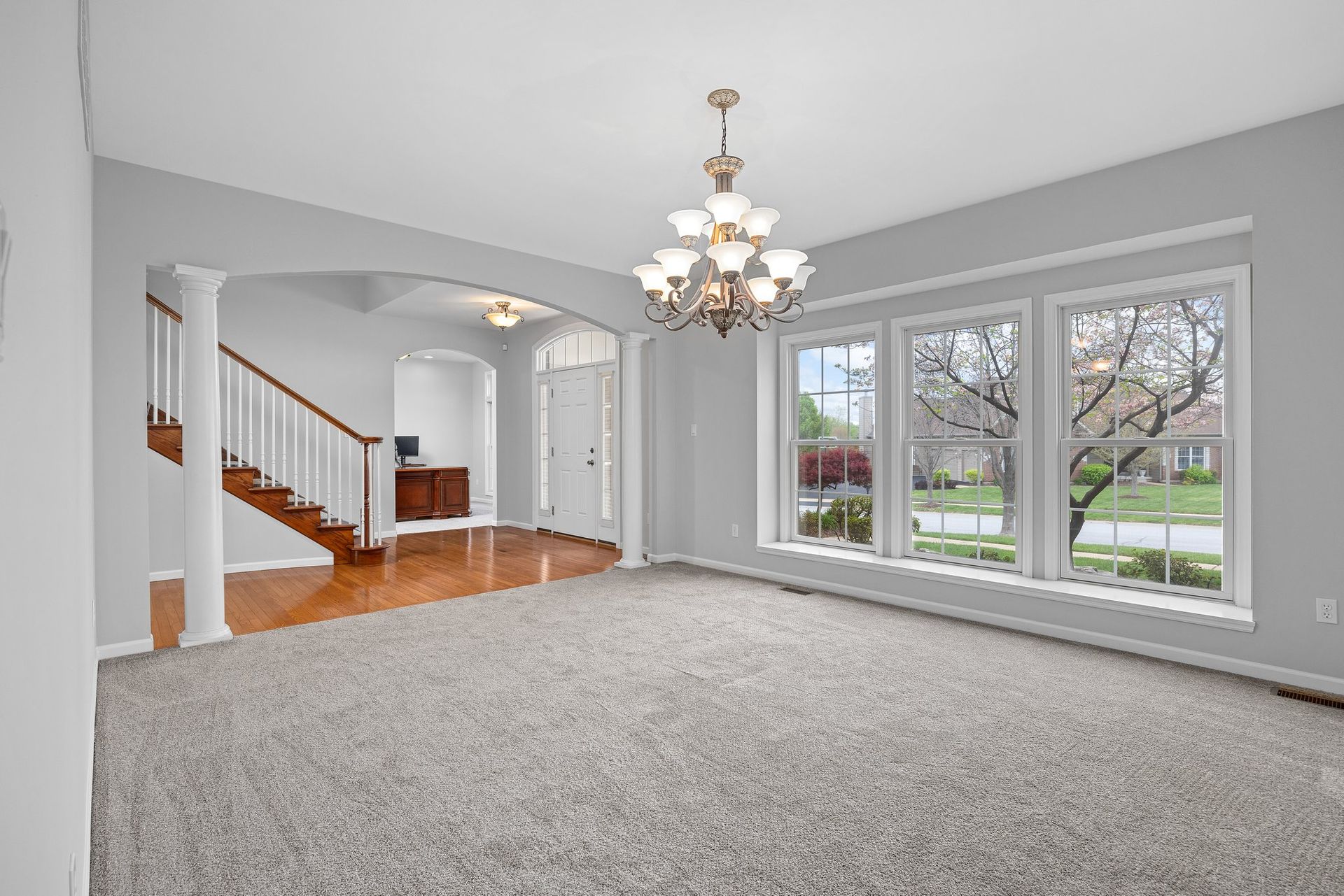 An empty living room with a chandelier and lots of windows.