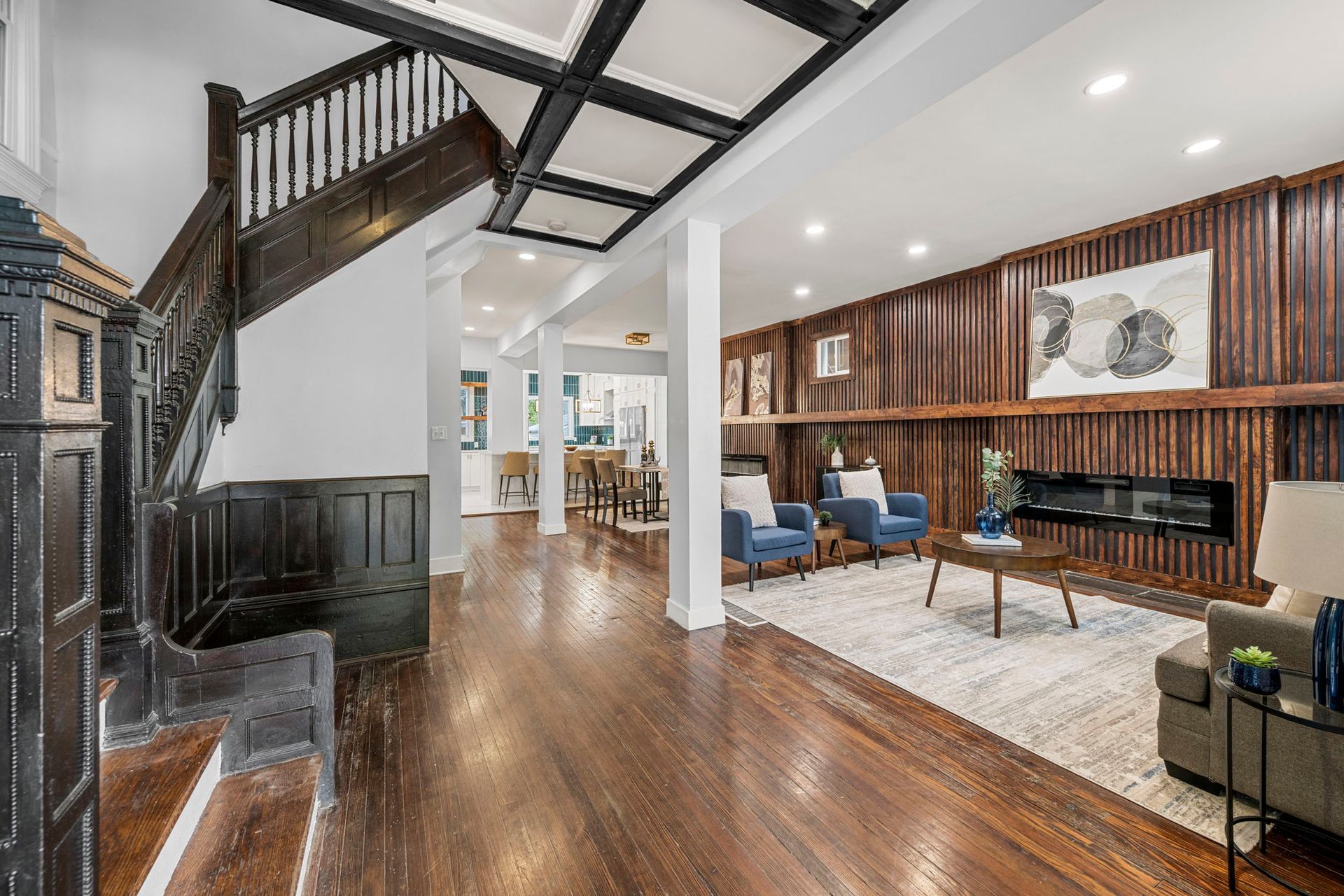 Interior of a house with hardwood floors, staircase, and a living room with a fireplace.