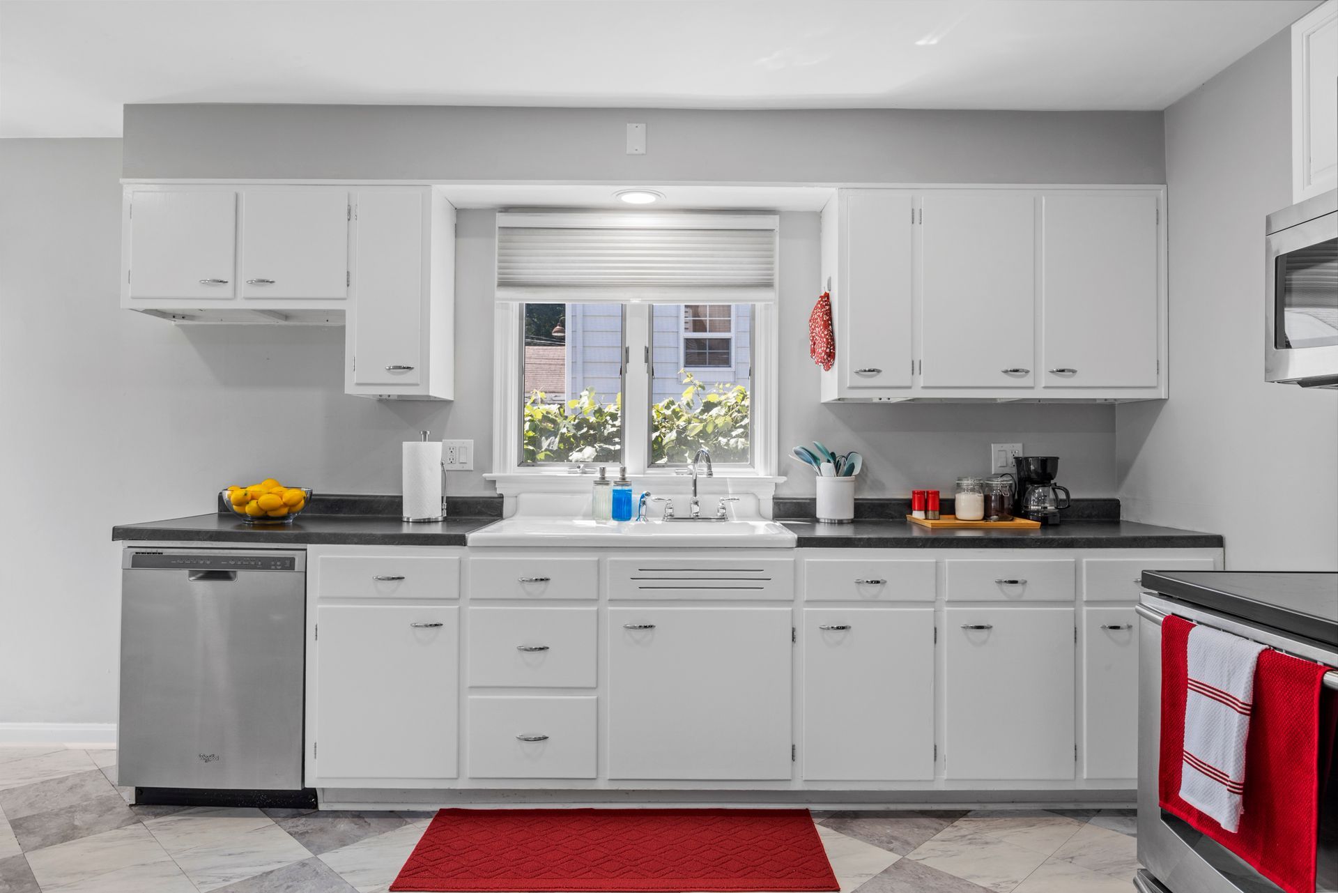 A kitchen with white cabinets , stainless steel appliances , a sink , and a window.