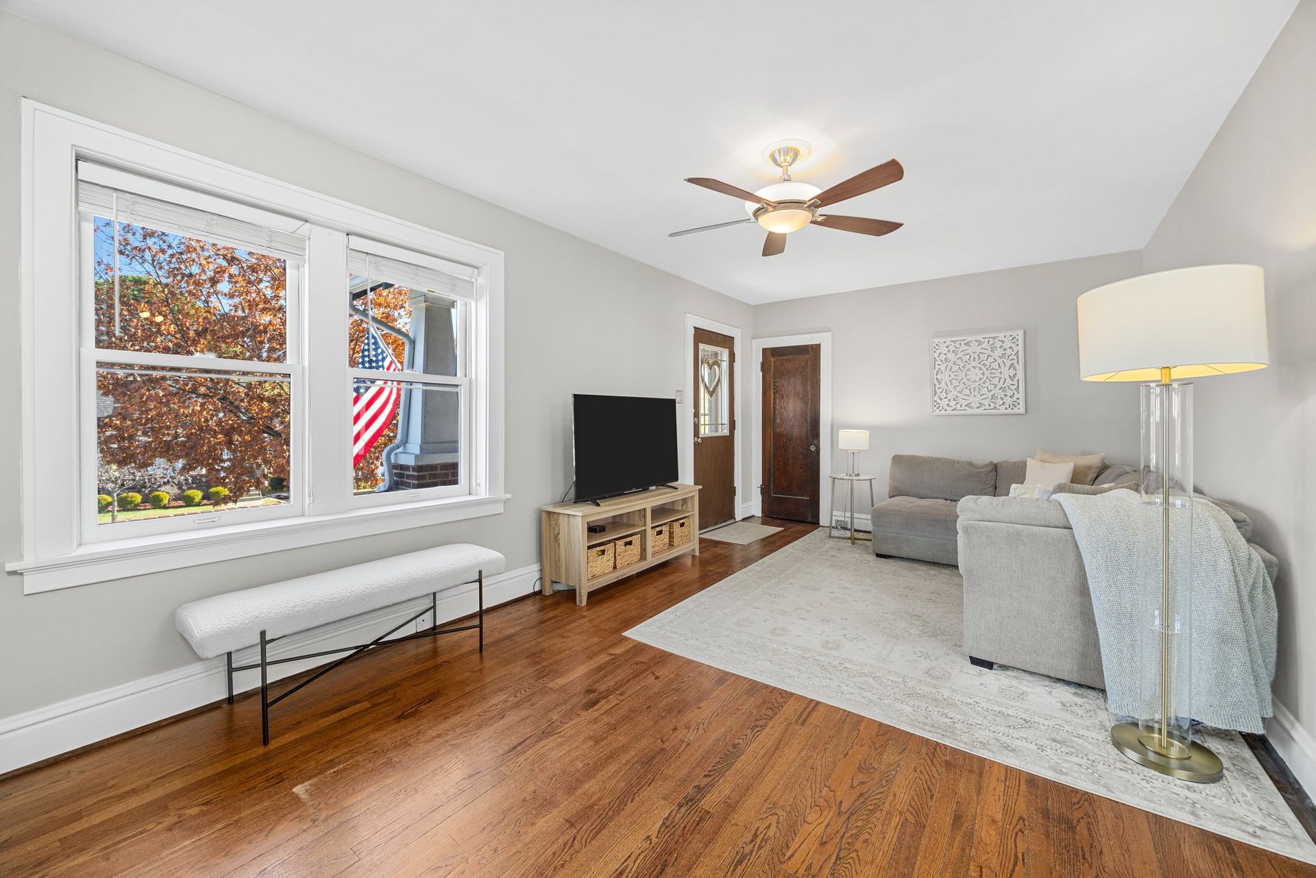 A living room with hardwood floors , a couch , a television and a ceiling fan.