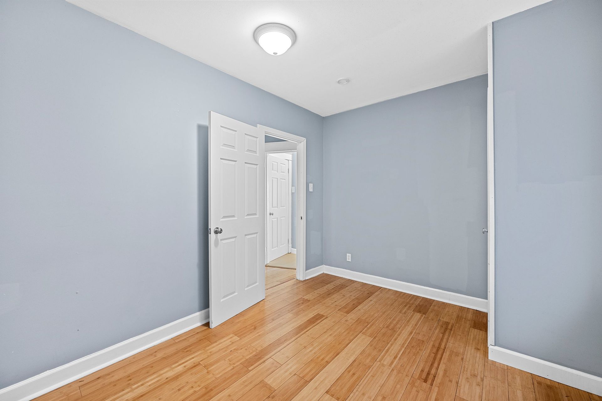 An empty bedroom with hardwood floors and blue walls.
