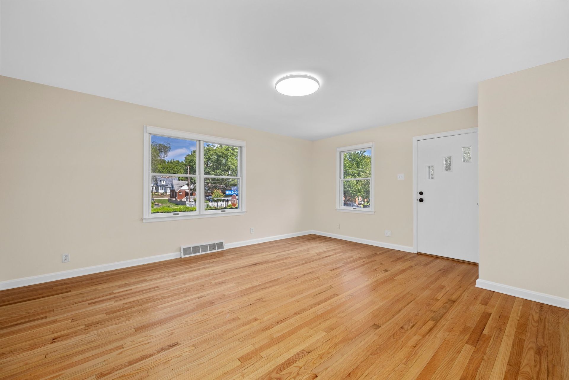 An empty living room with hardwood floors and two windows.