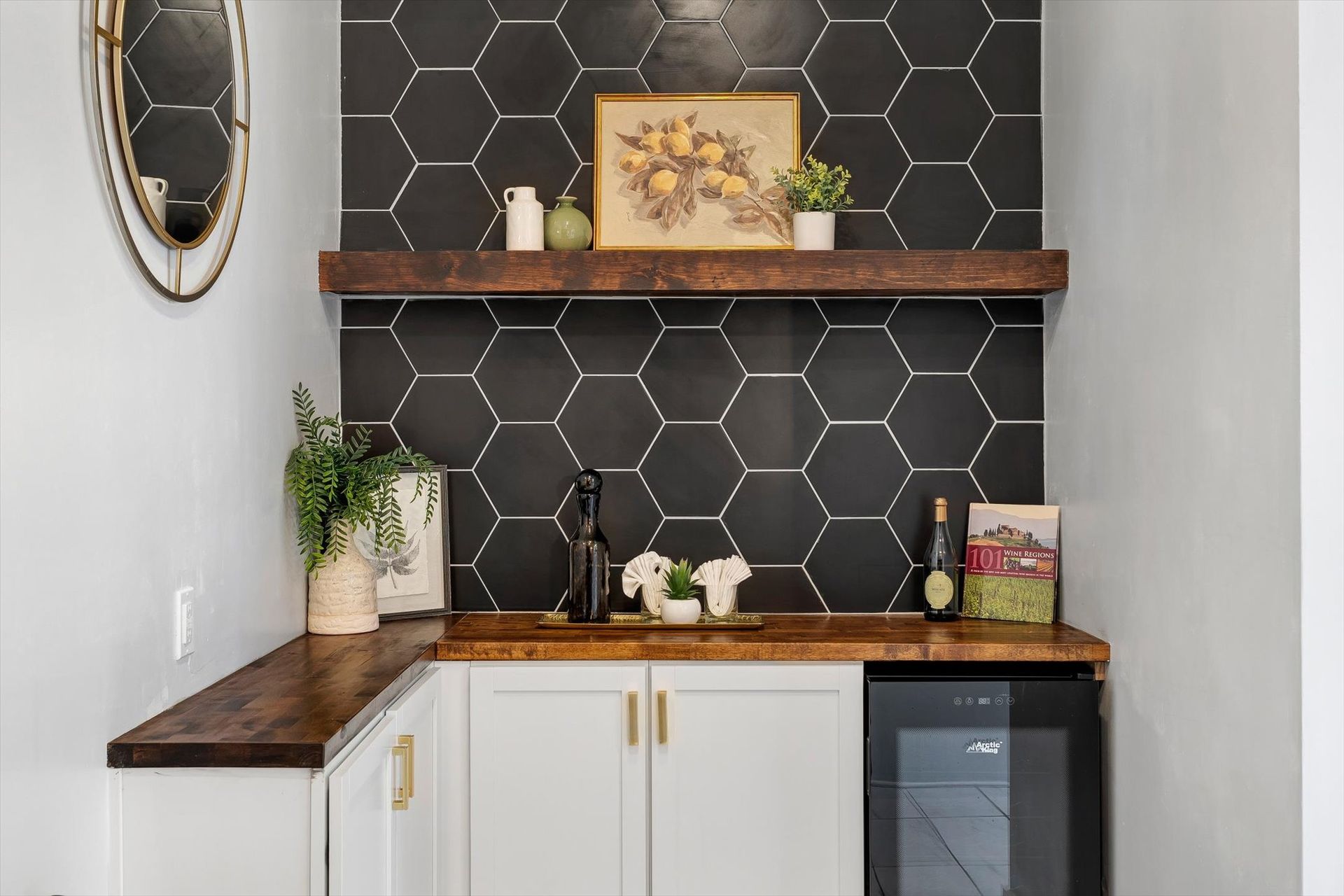 A built-in home bar with black honeycomb tile backsplash, wooden counter and shelf, white cabinets, and a wine fridge.