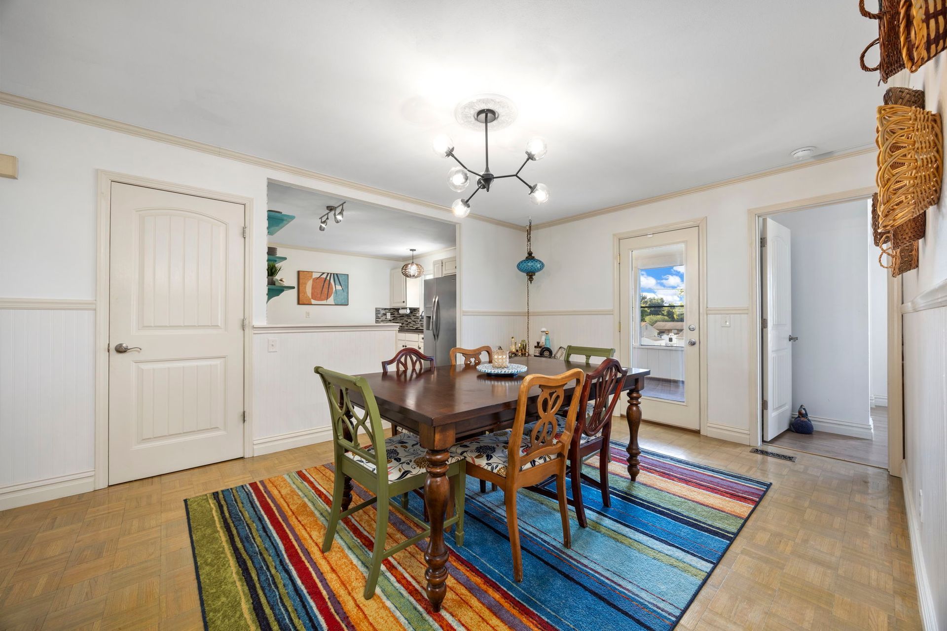 Dining room with wood table, colorful rug, mismatched chairs, and view of the outdoors.