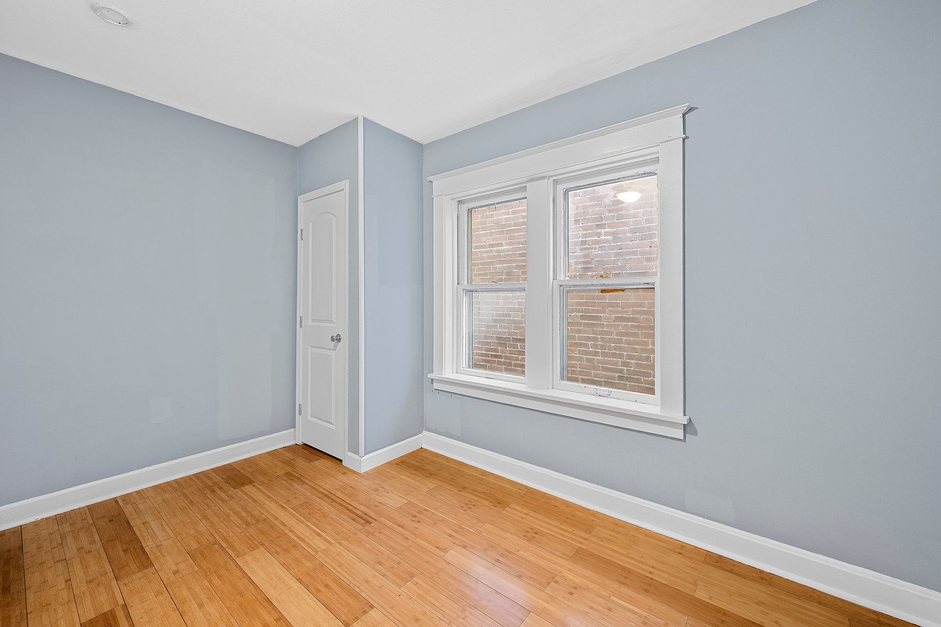 An empty room with hardwood floors and two windows.