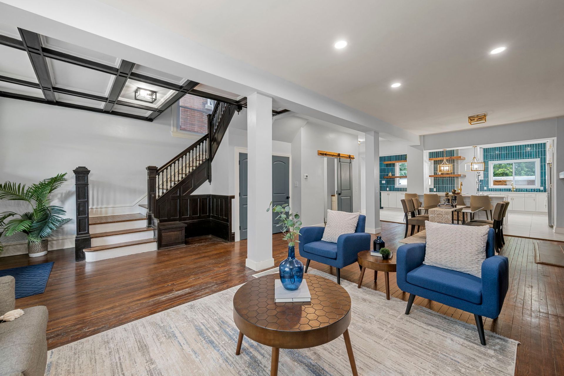 Living room with blue armchairs, wooden staircase, and dining area visible.