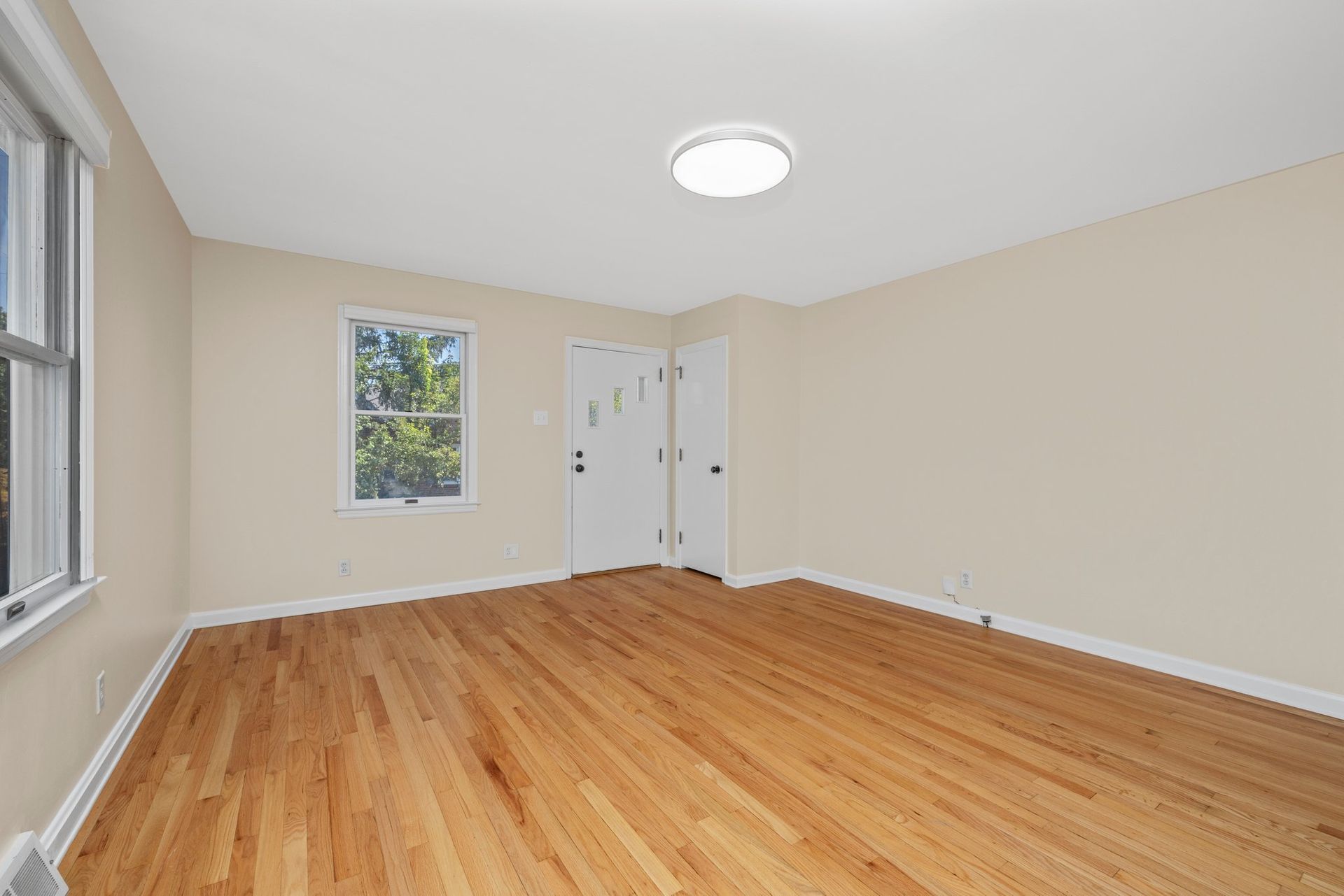 An empty living room with hardwood floors and a window.