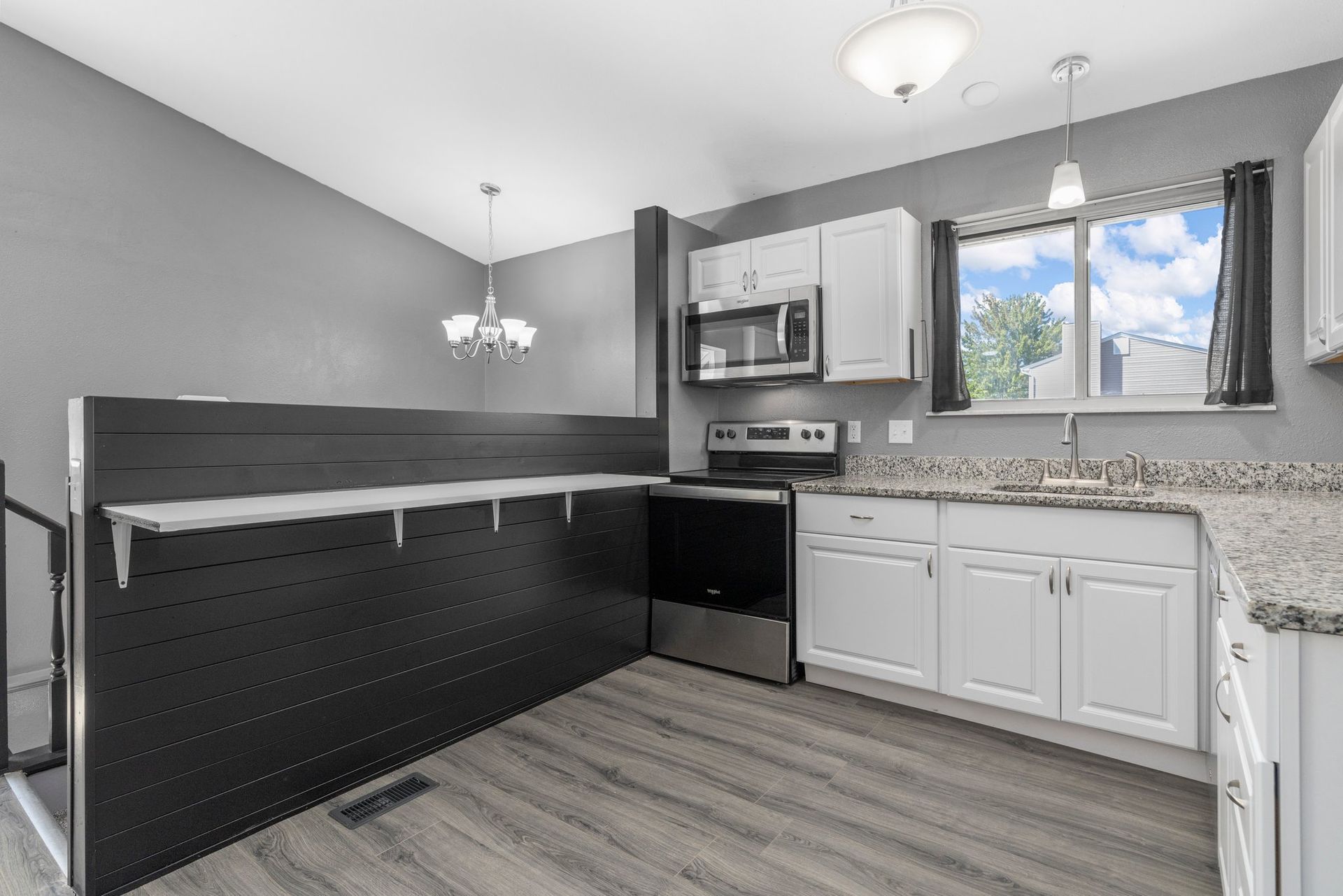 A kitchen with white cabinets , stainless steel appliances , granite counter tops and a window.