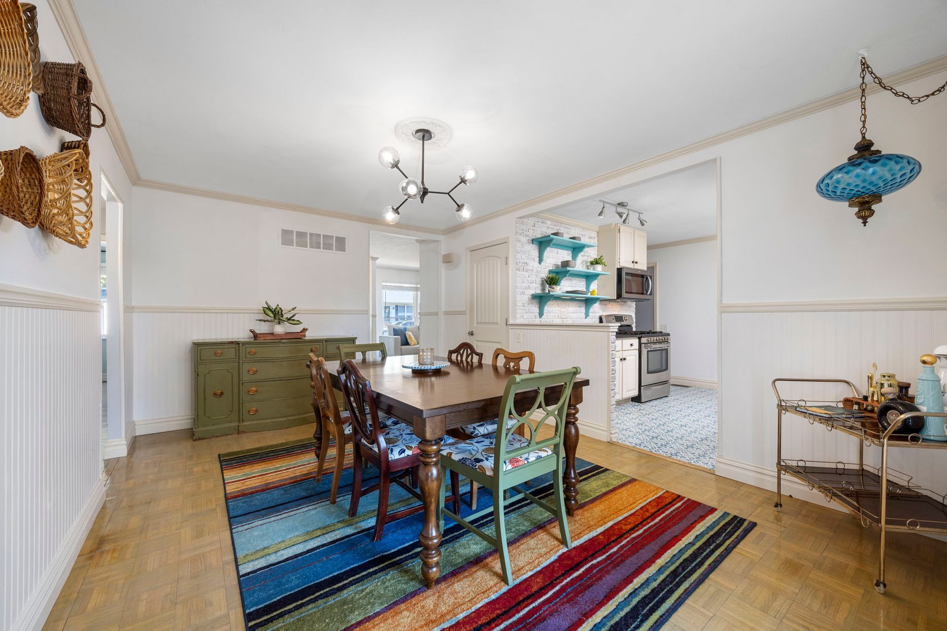 Dining room with a table, chairs, colorful rug, and open view to a kitchen.