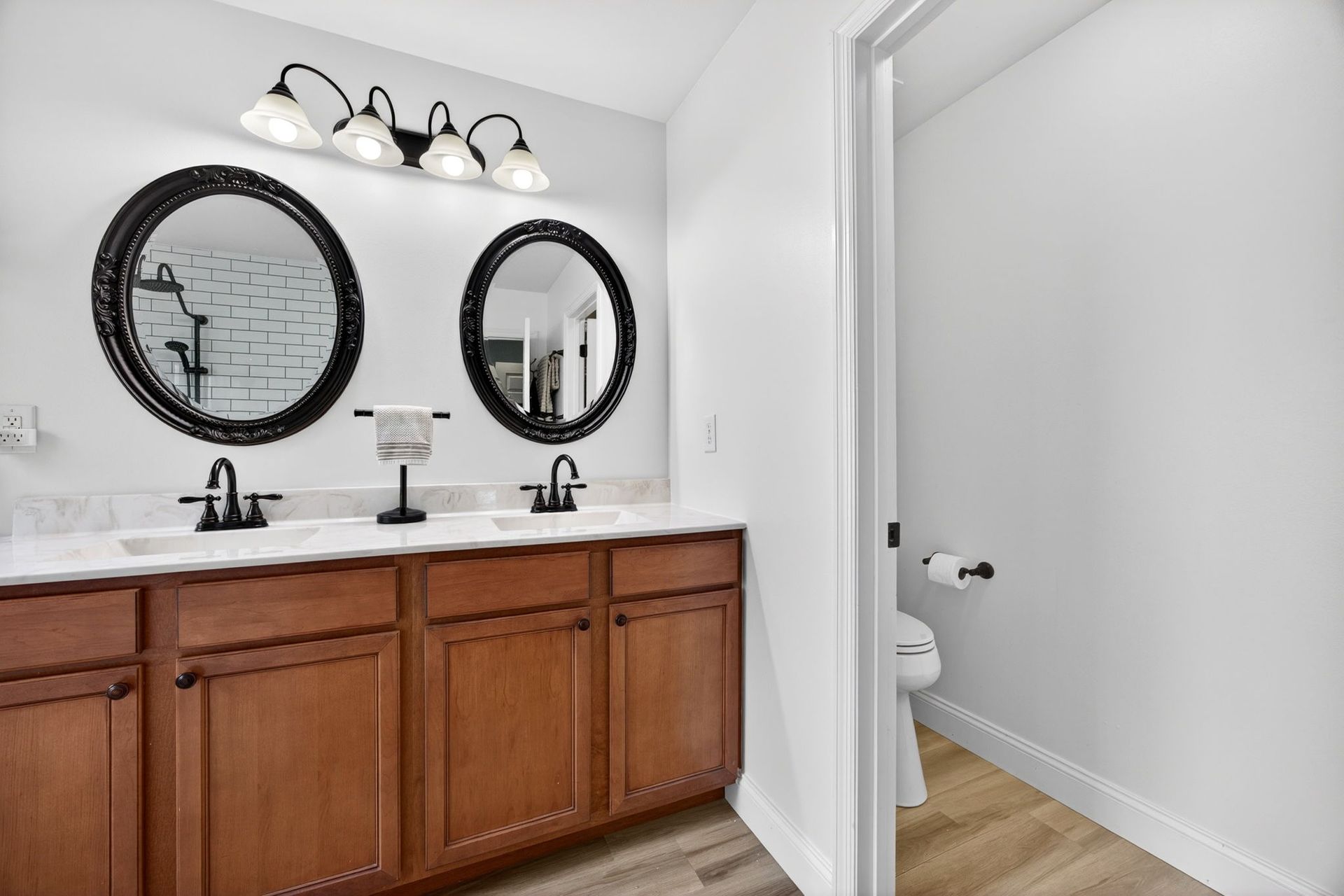 A double-sink bathroom vanity with wood cabinets, round mirrors, and a separate room with a toilet.