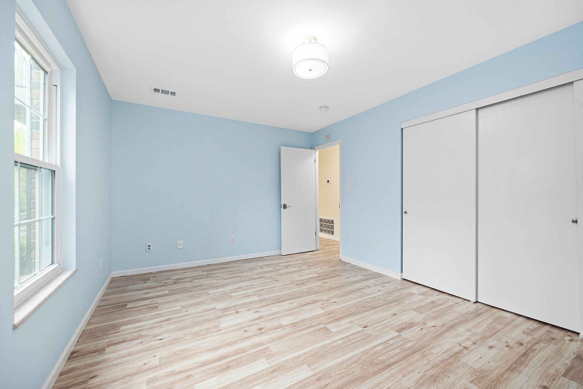 An empty bedroom with blue walls and wooden floors.