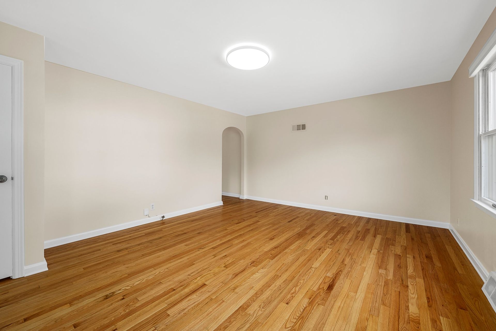An empty living room with hardwood floors and white walls.